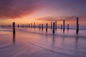 Gardinen Wooden poles on the beach at sunset © sara_winter