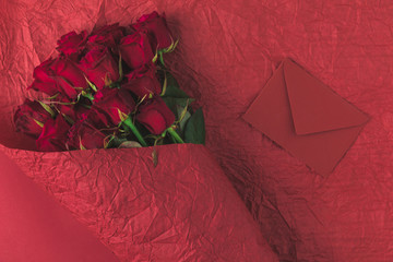 top view of bouquet of roses in wrapping paper and envelope isolated on red, st valentines day concept