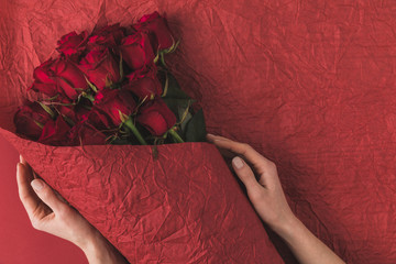 partial view of woman holding bouquet of red roses in wrapping paper for st valentines day