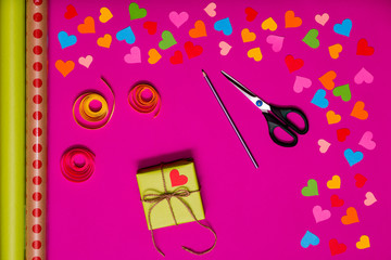 Valentines day gift wrapping with boxes over pink background and colorful paper hearts around. Process of handmade Present. Creative diy craft hobby. Holiday decorations