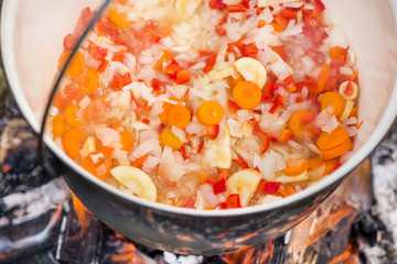 Boiling, hot goulash soup with meat, paprika, potatoes, onion, carrots is the traditional dish of Hungarian cuisine. Meat stew being prepared in crock pot on open fire. Picnic at the weekend in nature