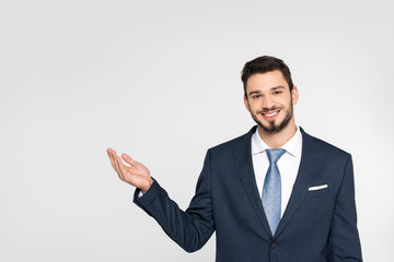 handsome young businessman showing copy space and smiling at camera isolated on grey