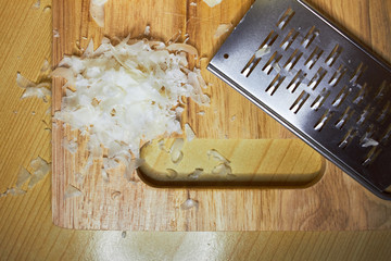 a slice of grated Parmesan cheese on a wooden cutting board beside a small iron grater for cheese. composition on a wooden surface