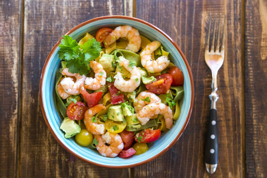 Noodle salad with avocado, tomato and shrimps in bowl on wood