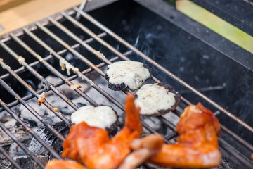 Mushrooms with cheese and chicken wings on barbecue grill on hot charcoal and fire. Spicy marinated chicken meat cooking over the flames. Preparing delicious food on holiday 