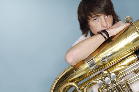 Portrait Of Teenage Boy With Tuba In Front Of Blue Background