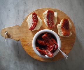 Slices of dried tomatoes dipped in oil in a jar and on pieces of bread. All on a round rustic ...