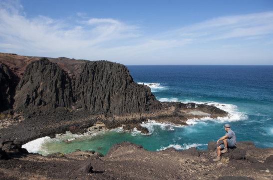 Spain, Canary Islands, Fuerteventura, Punta del mal Rayo, Agua Cabras, hiker sitting on stone