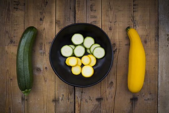Yellow and green zucchini and bowl of zucchini slices on wood