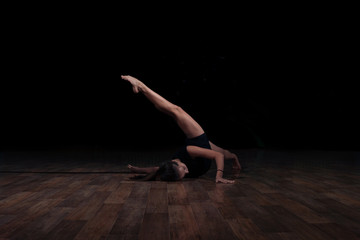 Flexible girl doing a gymnastic exercise on a black background. Sport. Fitness. Stretching.
