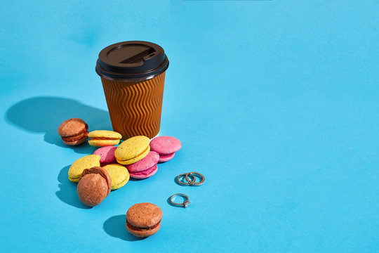 Hot coffee in brown paper cup with black lid and macaroons on bl