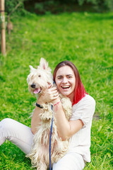 Young woman in grey clothes holding a dog while seating on the grass