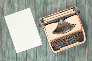 Retro old portable compact typewriter circa 70th and paper sheet blank on mint green grunge wooden desk. Vintage style filtered photo