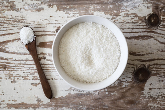 Coconut flakes in bowl, wooden spoon