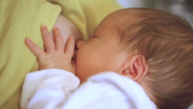 Newborn baby sucking his mother's nipple while eating
