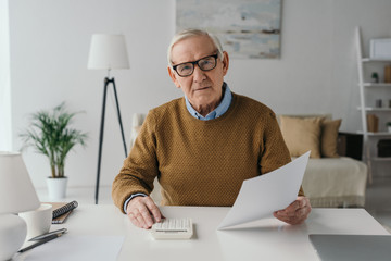 Senior smiling man using calculator and holding blank paper - Powered by Adobe
