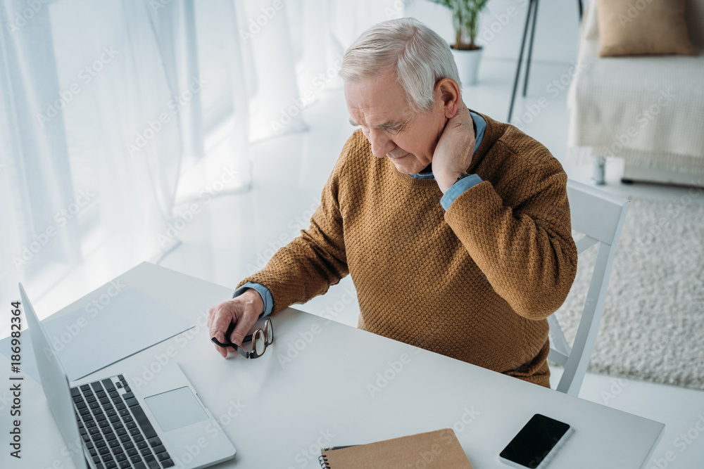 Wall mural Senior man working in office and suffering from pain in neck