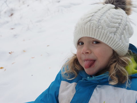 Fillette maline au bonnet blanc et boucles blondes tirant la langue