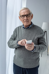 Senior confident man in eyeglasses using smartphone