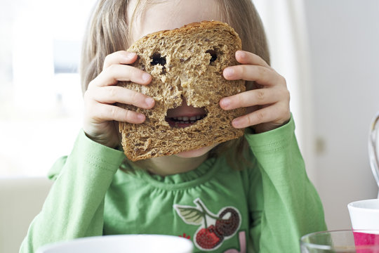 Little girl looking through holes in slice of bread