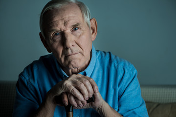 Senior man leans on a cane while sitting on sofa