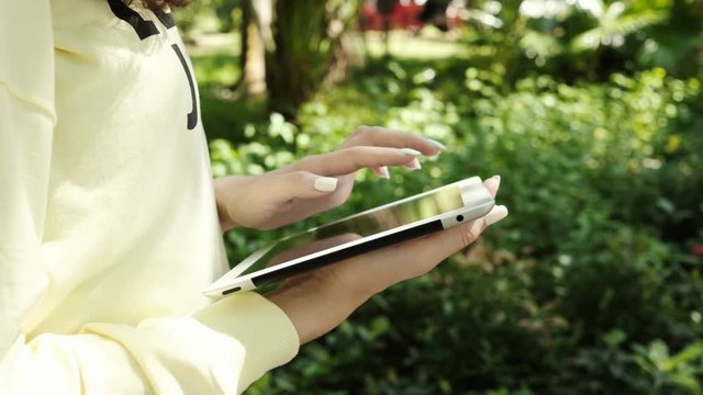 Closeup of young woman hands scrolling pictures phone. surfing internet. Business and communication anywhere in the world. Woman in a tropical park use a tablet