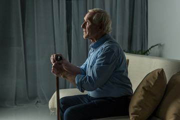 Senior confident man leans on a cane while sitting on sofa