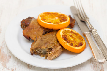 baked duck with orang on white dish with fork and knife