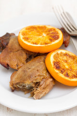 baked duck with orang on white dish with fork and knife