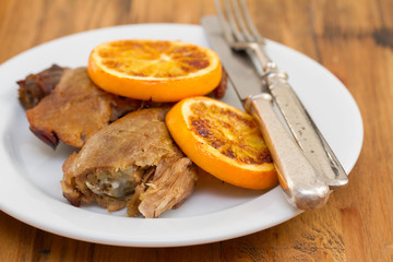 baked duck with orang on white dish with fork and knife