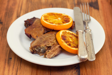 baked duck with orang on white dish with fork and knife