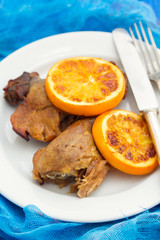 baked duck with orang on white dish with fork and knife