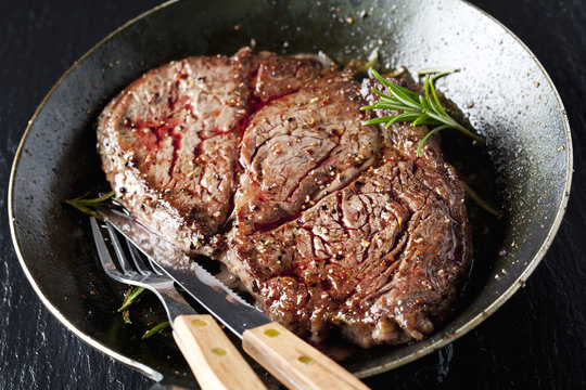 Rib eye steak with rosemary in frying pan