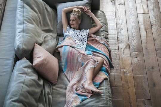 Woman relaxing on couch, wrapped in blanket
