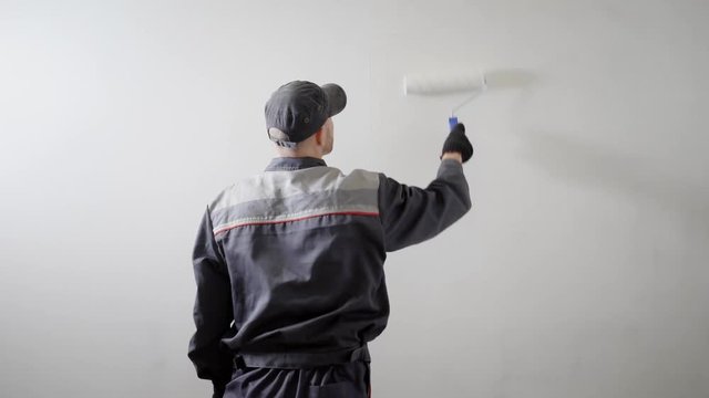 Shot from behind of a hired builder painting side wall in the new apartment in the building.
