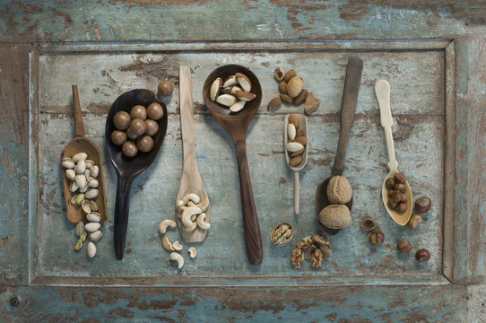 Row of spoons and shovels with different sorts of nuts on wood