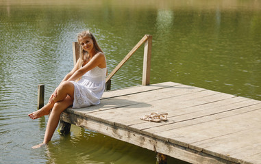 young girl wearing a white sitting by the river in summer afternoon.