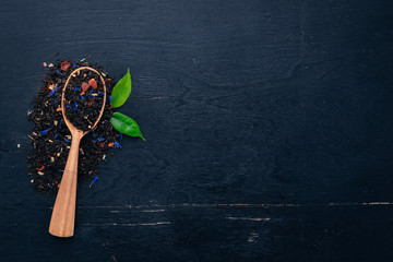 Black tea with flower petals of cornflower and dry berries. On a wooden background. Top view. Copy space.