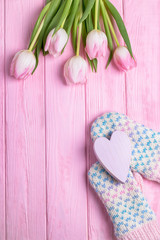 Happy Valentine's Day. Knitted gloves, wooden pink heart and pink tulips on a wooden background. Valentine's Day background. Top view, free space