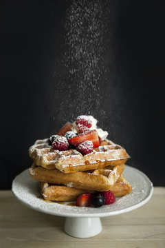Cake stand of Belgian waffles with different berries sprinkled with icing sugar