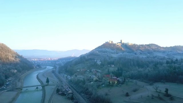 Aerial: Flying near city Celje in Slovenia over river Savinja on cold winter morning. Sun rising and shining on castle and city in background.