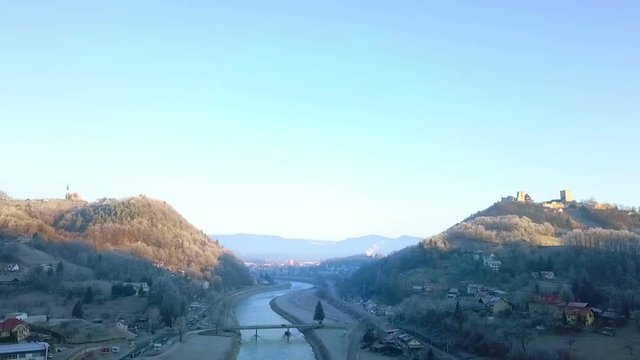 Aerial: Flying near city Celje in Slovenia over river Savinja on cold winter morning. Sun rising and shining on castle and city in background.