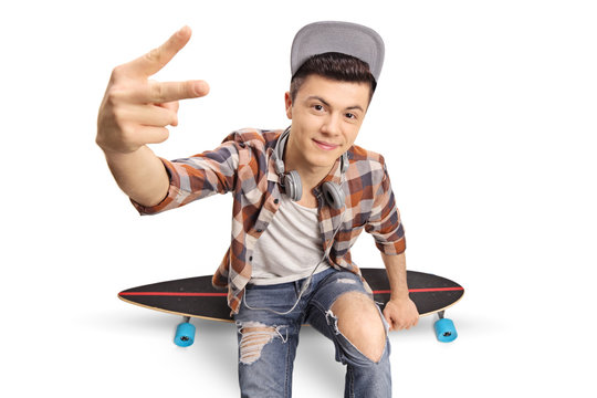 Teenage hipster sitting on a longboard and making a peace hand gesture