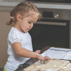 Little girl makes cookie from a dough in the kitchen at home