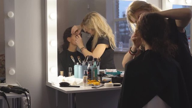 a professional make-up artist does the make-up of a young model. preparation of the model for the entrance to the podium. In the frame of the blonde and brunette 4k