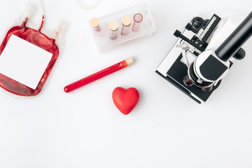 red heart against vials with blood and microscope isolated on white background