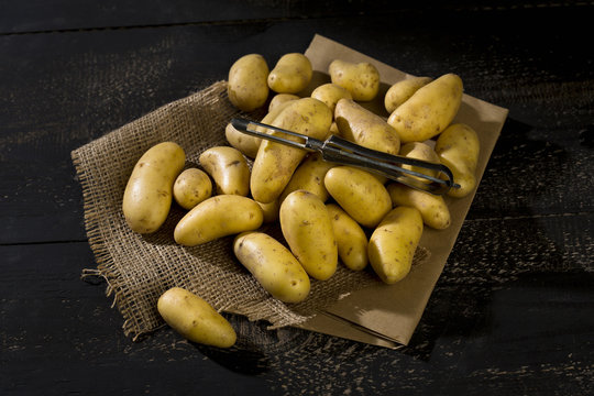 Raw Cherie potatoes and peeler on brown paper, jute and dark wood