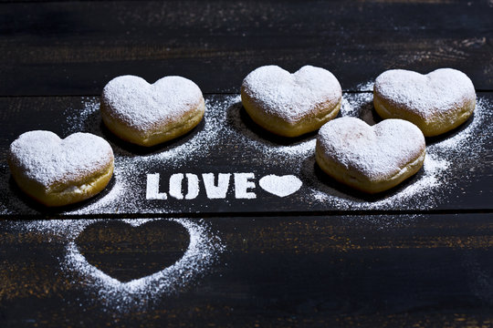 The word 'Love' stenciled with icing sugar and five heart-shaped crullers on dark wood