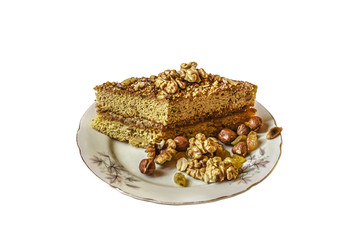 Piece of honey cake with nuts on a porcelain plate with raisins,hazelnuts,walnuts and peanuts on white background

