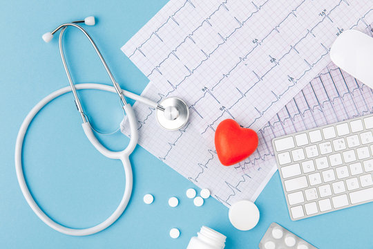 stethoscope, paper with cardiogram, scattered pills, red heart and keyboard isolated on blue background